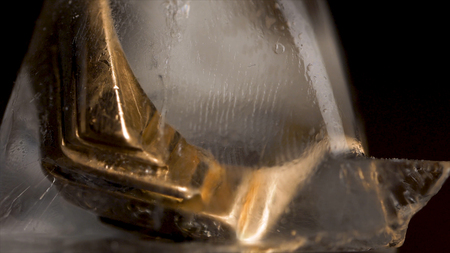 Golden ring in ice cube isolated on black background. Gold in ice cube. Golden ring with ice cubes on wooden table and black backgroundの写真素材