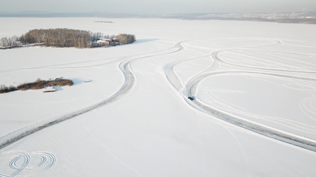 One car driving through the winter forest on country road. Top view from drone. Aerial view of snow covered road in winter, car passing by. Top view of the car traveling on snowy road.の写真素材