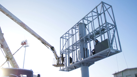 Builder on a Lift Platform at a construction site. Men at work. construction worker assembling scaffold on building site. Men assemble Billboard on tap.の写真素材