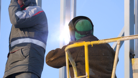 Construction workers working on scaffolding, Man Working on the Working at height with blue sky at construction site. Worker using electric wheel grinding on steel structure in factory. Work on high.の写真素材