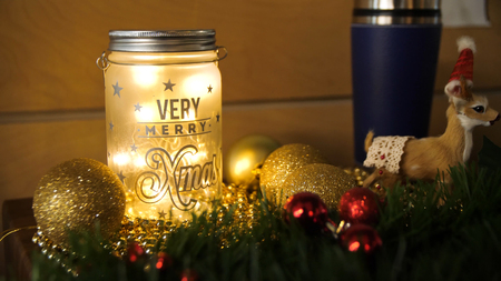 Christmas candles with Christmas tree decorations and a white candlestick house, white and blue and tree branches with a Christmas garland on a wooden table. Christmas toys on the table and the candlestick.の写真素材