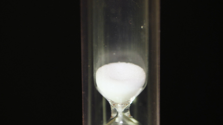 Hourglass. Time Passes - Glass hourglass with white sand on black background. Classic Style Vintage Old Hourglass Sandglass Clock. Macroの写真素材