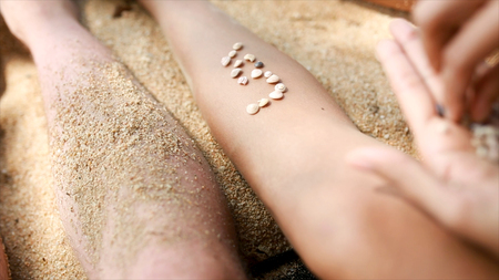Female hands collect pattern of shells and sand, close up. Video. Pieces of amber and seashells in...