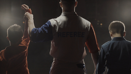 Rear view of the boys athletes and referee who raises the hand of the winner. The referee raises the hand of the boy winner in the ring. Judoの写真素材