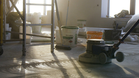 Builder polishing mortar floor at construction site of new appartments. Mechanized grout screed concrete floor close-up. Laborer performing and polishing sand and cement screed floor.の写真素材