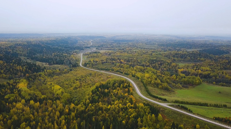 Aerial view of unlimited space of forest plain and cars which are riding on highway. Clip. Road in the autumn forest aerial view. aerial view over road between forestsの写真素材