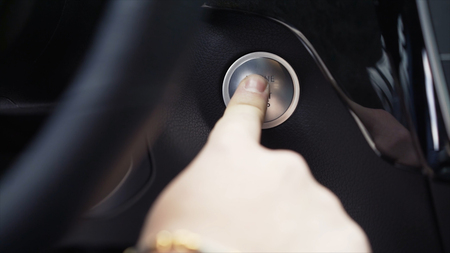 Driver hand pushes engine start stop button. Stock. Modern luxury crossover car interior details.