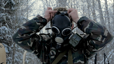Man in uniform wearing a gas mask in the winter forest. portrait of a young soldier wearing a gas mask against a nature background.の写真素材