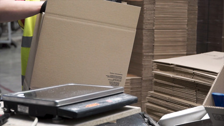 Close-up view of the hands of a manufacturing worker putting packed products in cardboard boxes, before export or shipping during manual work in a cosmetics factory. Clip. Worker in warehouse preparing goods for dispatch. Warehouse worker preparing a shipment in a large warehouseの写真素材