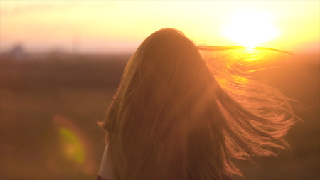 Portrait of beautiful long-haired woman against background of sunset rays of sun. Charming woman with hair fluttering in wind in rays of sunsetの写真素材