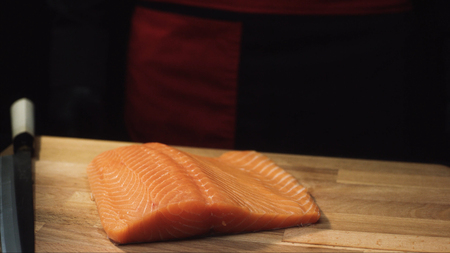 Close-up of raw salmon fillet on wooden board with knife. View of juicy piece of salmon before cutting to prepare delicious dishの写真素材