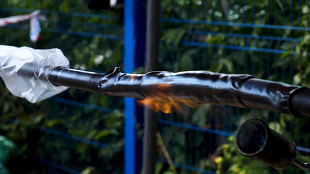 Blowtorch. Frame. Close-up of work with blowtorch on street on background of trees. Roasting of pipes with gas burner.の写真素材