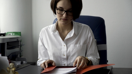 Close up for young woman in white shirt looking at laptop, answering the phone, and smiling on white office wall background. Businesswoman working in front of computer screen in her working place.の写真素材