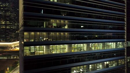Singapore - 25 September 2018: Bright and beautiful lights reflection in night windows of business building with glass facade. Shot. Beautiful lights reflection at night, windows office building background.のeditorial素材