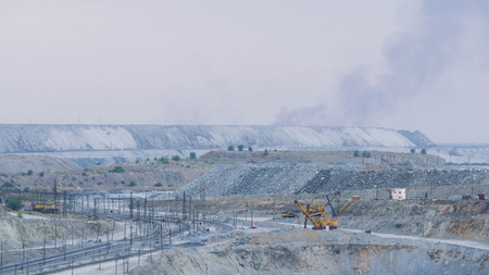 Panorama of an open quarry. Mining industry. Large quarry excavator in the background of hills of cruched stone next to a mining enterprise, panorama. Mining equipment. Panorama of a large quarry for limestone mining in sunny weather.の写真素材