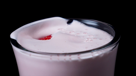 Close-up of glass with strawberry milkshake. Frame. Freshly whipped pink milkshake in clear glass on...