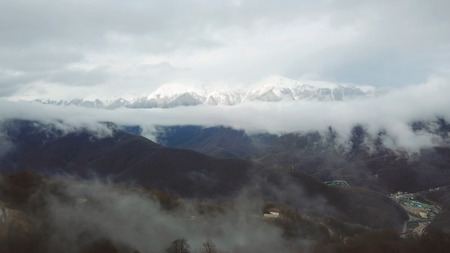 Top view through clouds on snowy peaks of mountain valley. Beautiful landscape of mountain peaks...