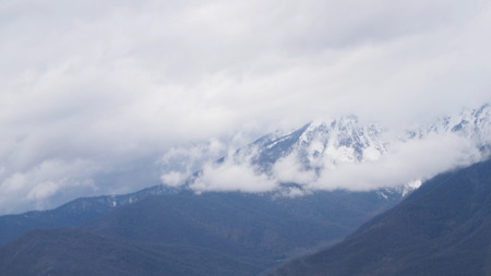 Top view of mountain landscape and small winter resort. Gloomy clouds looming over mountain peaks and foothills of winter resort in snowy weather.の写真素材