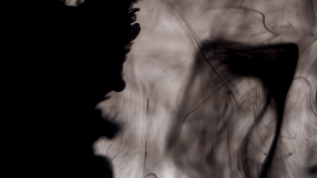 Close-up of black ink in water on white background. Drops of black ink beautifully splash in water, creating abstract art background.の写真素材