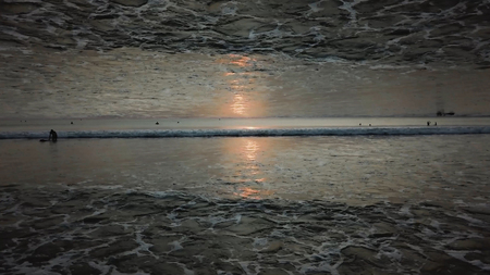 Stunning sunset sky above the ocean with a mirror horizon effect, view from the shore. Endless waves and people in water, inception theme.の写真素材