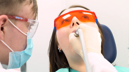 Professional dentist working with patient in modern clinic, medicine concept. Media. Young patient in protective glasses while teeth treating process.の写真素材