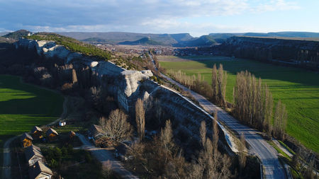 Aerial view of stunning natural stone wall, high and long cliff with growing trees and green fields on each side of it. Shot. Beautiful landscape with high mountains and a village in the valley.の写真素材