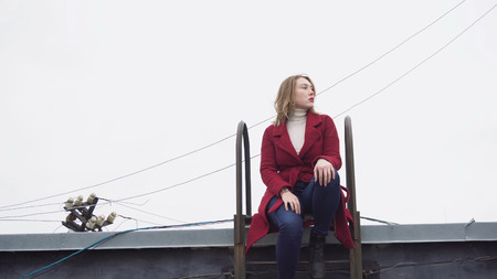 Model sitting on roof in winter. Media. Attractive young woman model posing sitting on roof with...