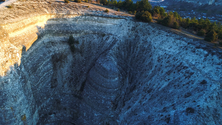 Top view of stone cliff with green bush at peak. Shot. Beautiful mountain landscape with rock casting shadow from evening sun and separating dark and light sidesの写真素材