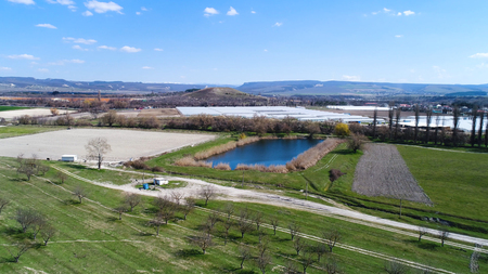 Aerial for a small pond surrounded by bushes and hills in the mountainous countryside. Shot. Beautiful landscape with green meadows, small rare trees on blue cloudy sky background.の写真素材