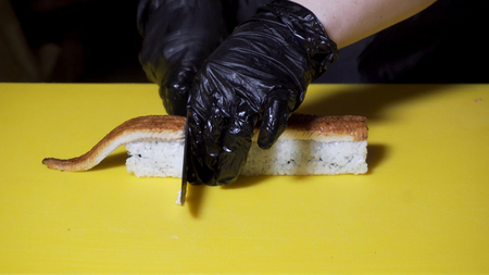 Close up for knife in hand cutting the roll on a yellow board, asian food and cooking concept....