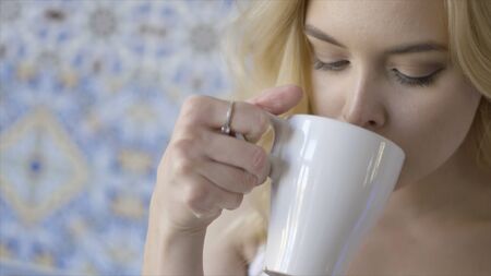 Beautiful blue-eyed young blond woman drinking tea. Action. Young beautiful lady with ring on her...