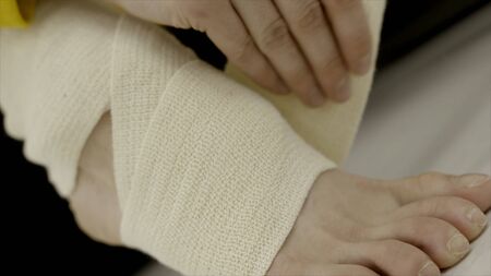 Close-up woman bandaging her leg with elastic bandage. Action. Unexpected injury or stretching of ankle while exercising and applying elastic bandageの写真素材