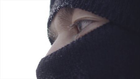 Close-up sad look of young man in winter. Action. Dramatic bored look of young man, turned to side covered with frost. Look of guy from under the winter Balaclavaの写真素材