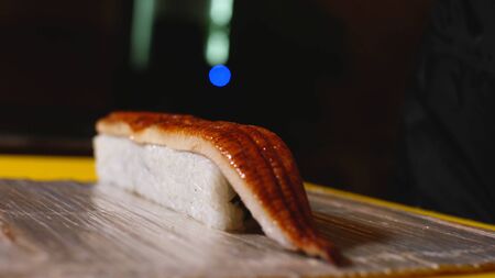 Close-up of chef preparing sushi roll with fish. Frame. Professional chef in gloves puts piece of eel on sushi rolls. Preparation of aesthetic and delicious sushi rollsの写真素材
