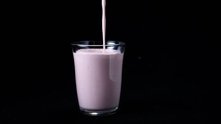 Strawberry milk shake isolated on black background. In transparent glass pour viscous pink milkshake on black background. Cool milkshakesの写真素材