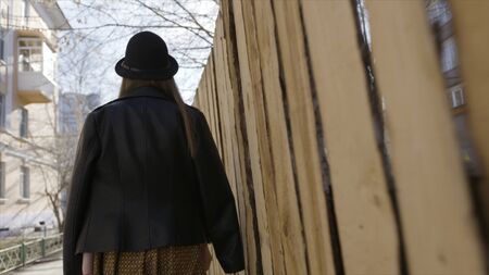 Rear view of a young beautiful model girl in wide-brimmed hat and black leather jacket walking in the city. Action. Dynamically young girl walks down the street with her fair fluttering in the wind.の写真素材