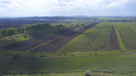 Aerial drone view of ploughed and green fields, trees, small town with blue cloudy sky on the...