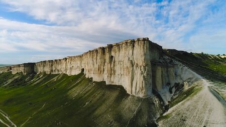 Top view of beautiful white rock with green grass on background of blue sky. Shot. Panorama of white cliff with green field at foot of summerの写真素材
