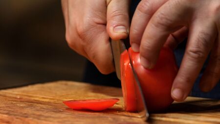 Cutting red tomato on wooden board. Stock footage. Chef cut tomato on a wooden Board