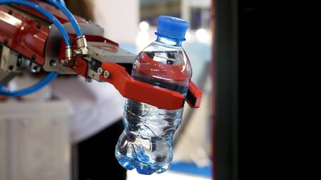 Close up for the red robot hand holding a bottle of wate on blurred background, artificial intelligence concept. Automatic industrial machinery equipment.の写真素材