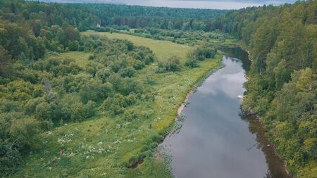 Beautiful view of Russian river near green meadow covered with shrubs, flowers and trees and forest...