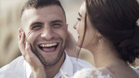 Close-up of young and lovely newlyweds kissing. Action. Sincere and radiant smiles of bride and...