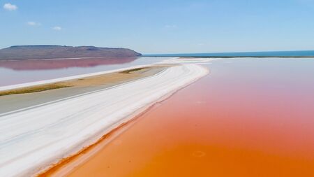 Orange lake in Crimea. Shot. Top view of bright orange lake water against white sand. Extraterrestrial landscape of colorful orange water on white sand on background of blue skyの写真素材