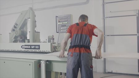 Worker working at sawing machine in production. Action. Worker controls process of cutting wooden board on automated machine. Modern automated equipmentの写真素材