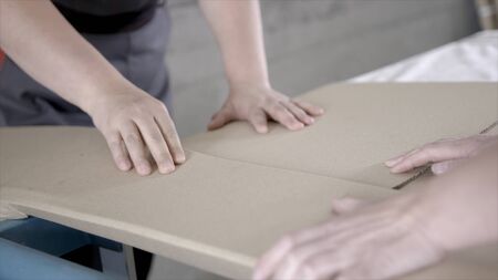Close-up of workers packed flat package. Action. Workers in overalls pack building material from factory for home delivery. Building materials or furniture are delivered directly from factoryの写真素材