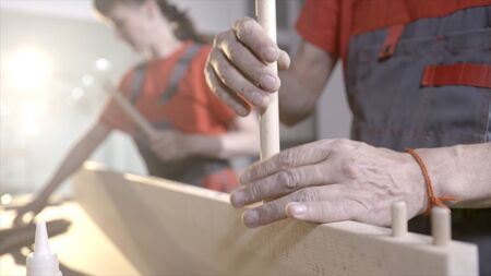 Wooden furniture mounts. Action. Close-up workers put wooden dowels in frame. Connection of wooden furniture details. Fixing furniture with round wooden sticksの写真素材