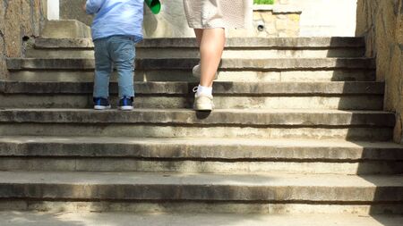 Close up of woman helping her little child boy to climb the stairs by holding his hand. Stock footage. Mother with small kid son walking up the stairs.の写真素材