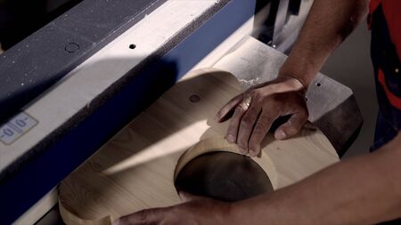 Close-up of man grinds wood products on industrial machine. Action. Carpenter polishes wooden...