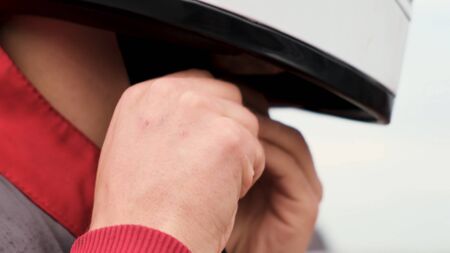 Extreme close up of a man trying to take off white protective helmet on bright sky background. Media. Young man is trying to unfasten his safety helmet to take it off.の写真素材
