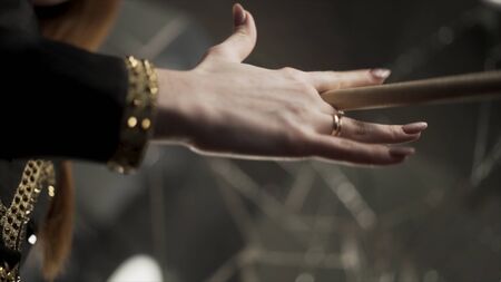 Young attractive woman hand holding drumstick and rotating it during musical rehearsal. Action. Close up for woman hand with manicure and gold rings holding and spinning a drumstick.の写真素材